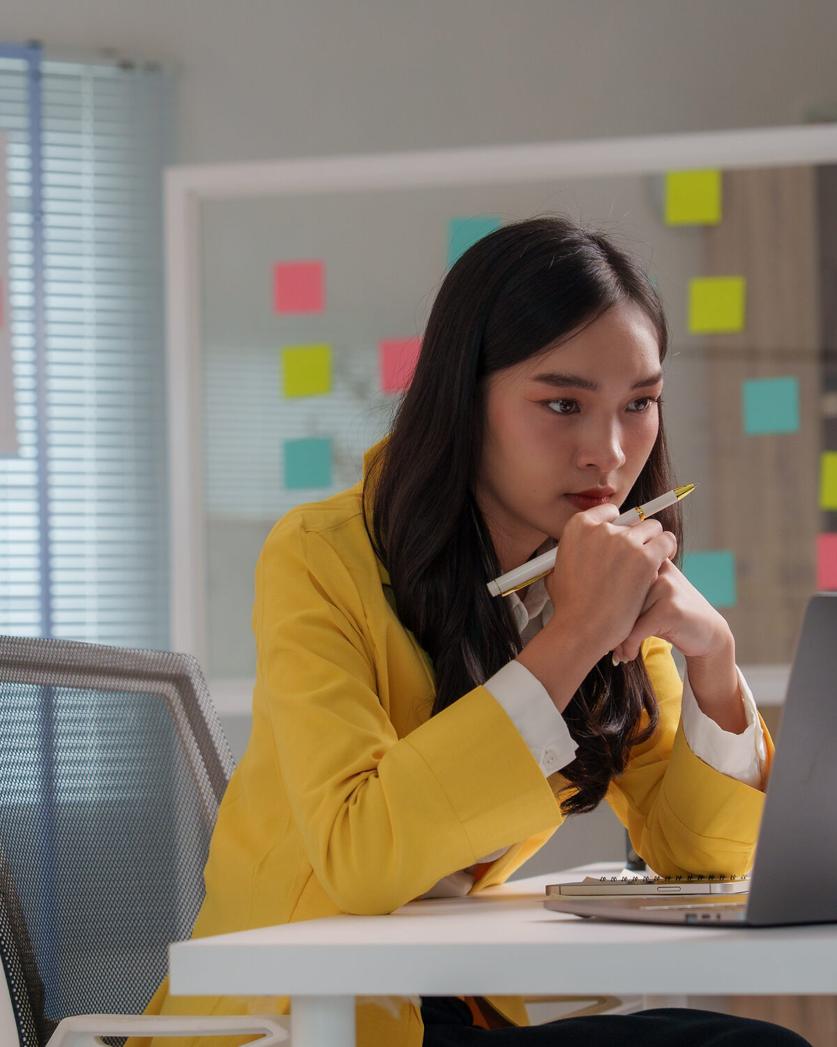 A focused woman working at a laptop in a calm, sunlit office.