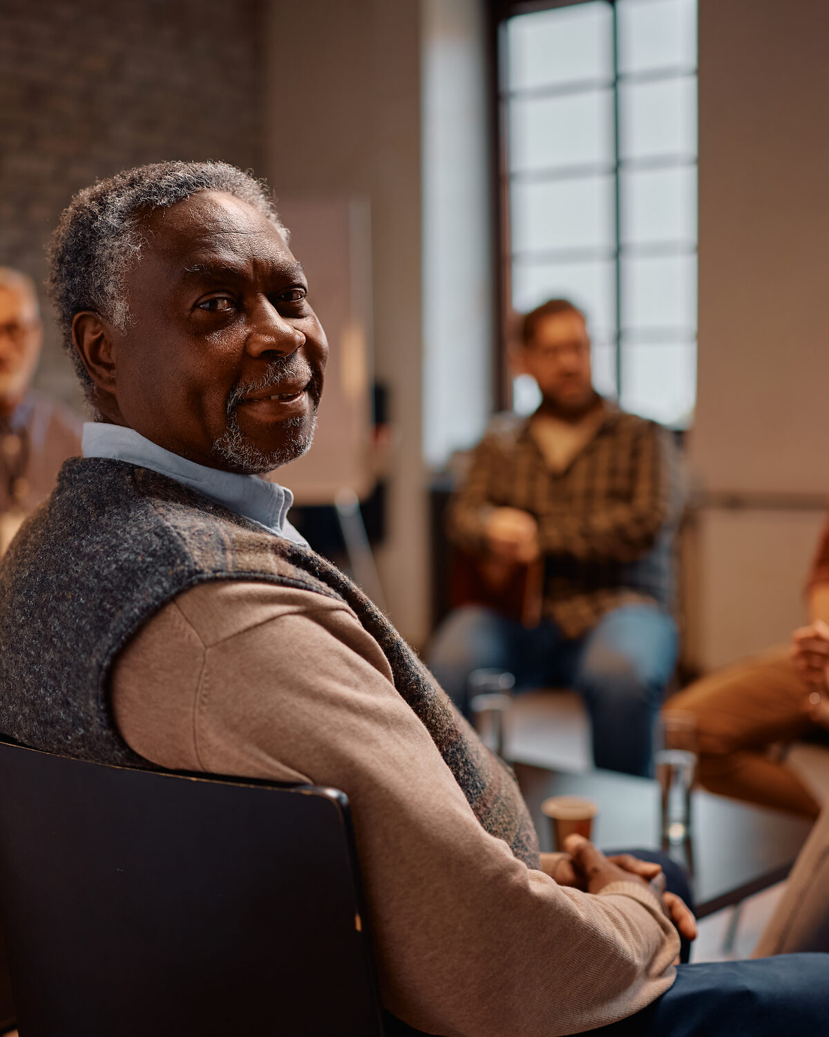 An older man sitting in a thoughtful pose, listening attentively in a quiet, lit space.