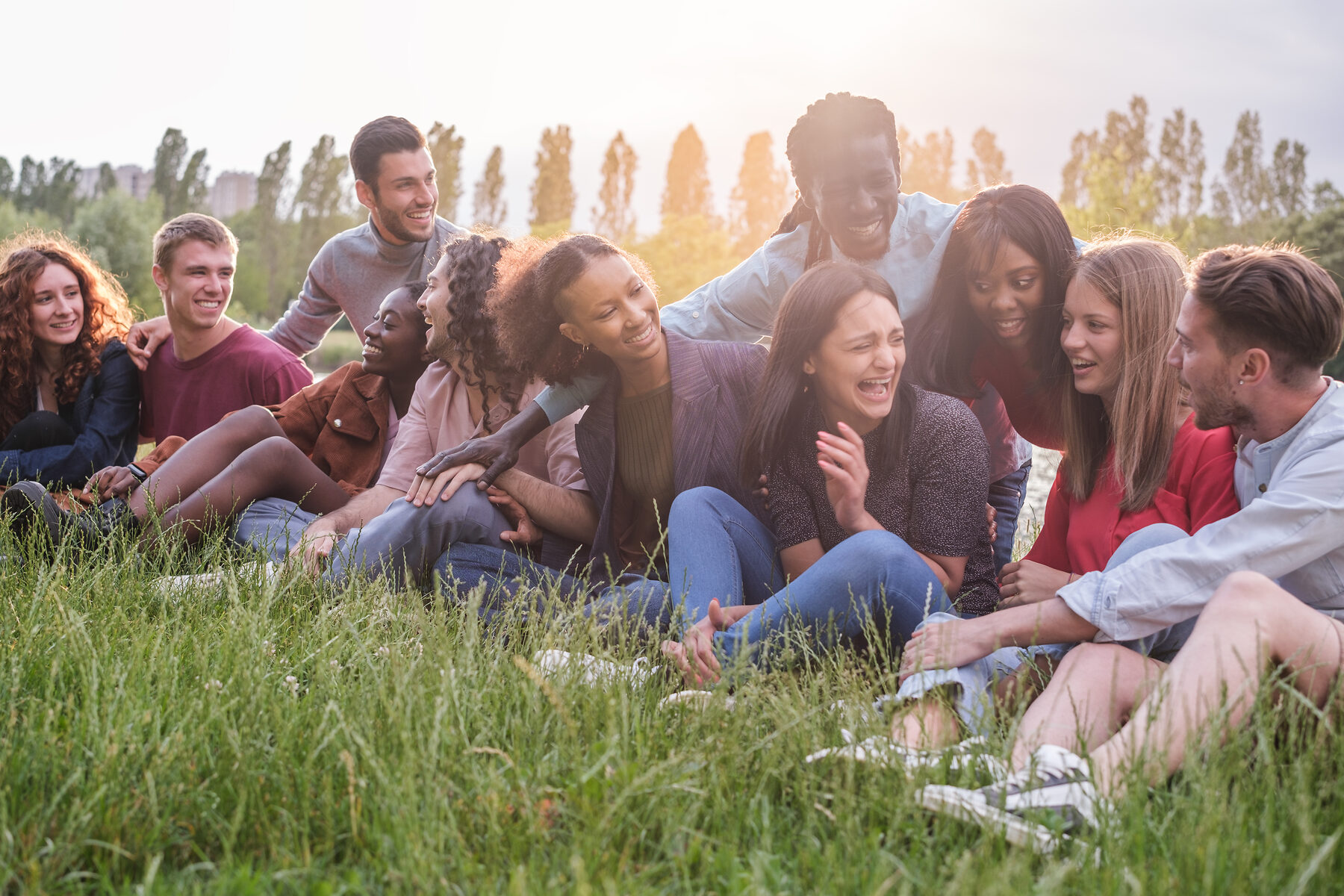 Un grupo diverso de amigos sentados juntos en el césped de un parque, conversando bajo la luz suave de la tarde.